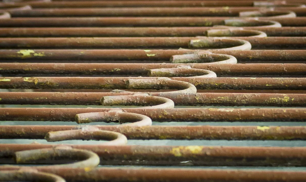 Rows of rusted curved rods repeating across a flat surface